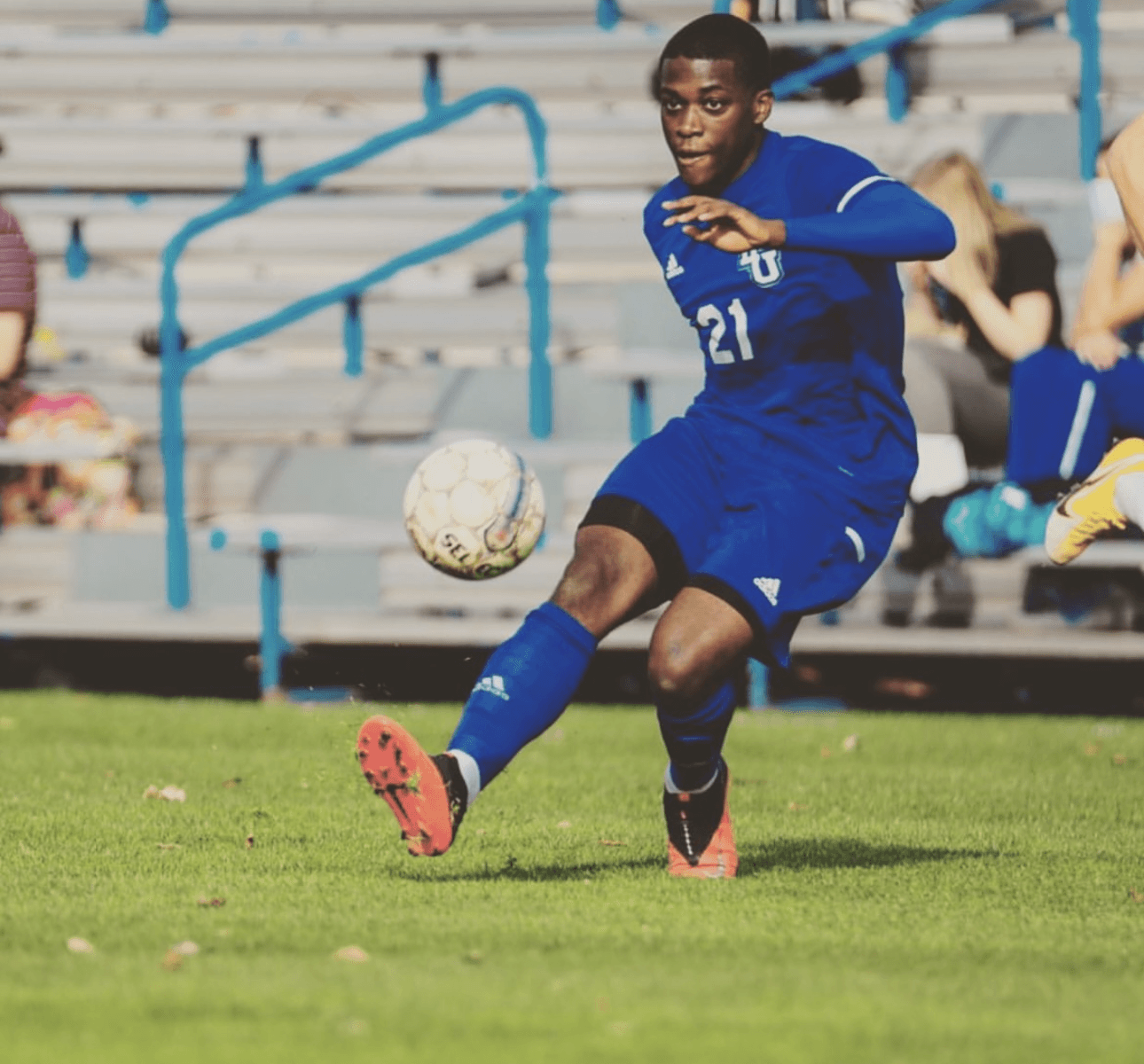 Student-athlete in a blue kit striking a football during a match